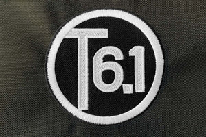 T6 point 1 embroidered circle logo with white text over a black background