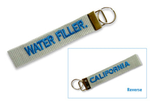 A grey fabric key ring with water filler embroidered on one side in blue and california embroidered in blue on the reverse.