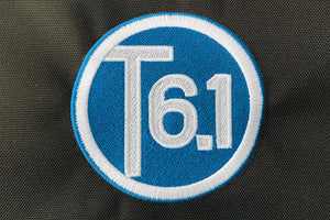 T6 point 1 embroidered circle logo with white text over a blue background