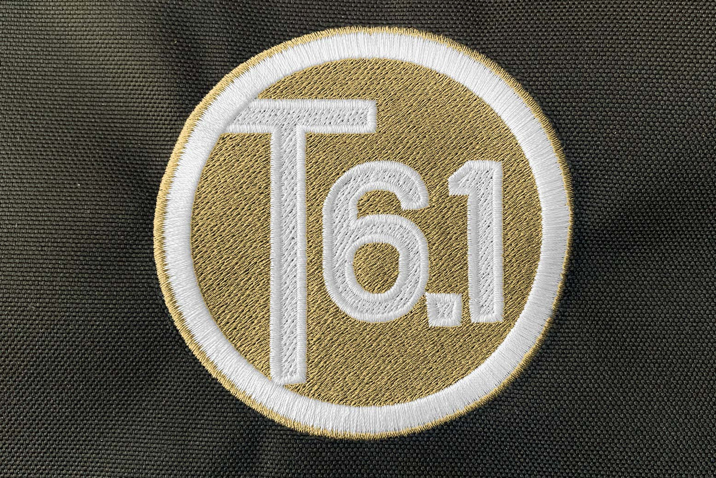 T6 point 1 embroidered circle logo with white text over a cream background