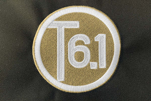 T6 point 1 embroidered circle logo with white text over a cream background