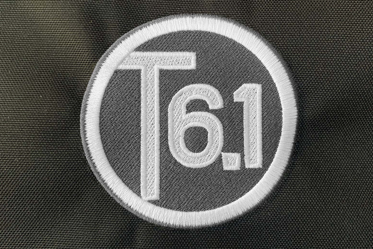 T6 point 1 embroidered circle logo with white text over a grey background