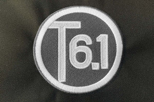 T6 point 1 embroidered circle logo with white text over a grey background